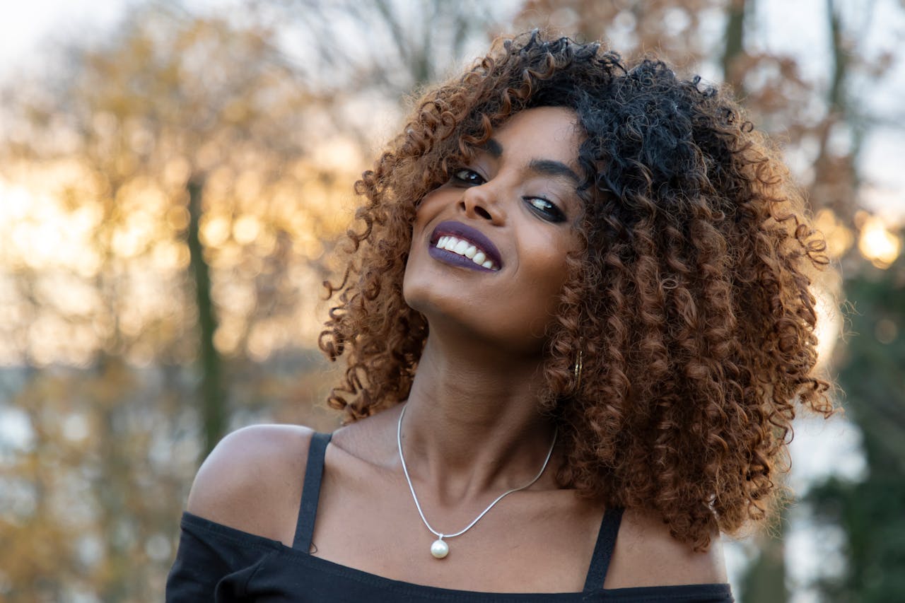 Portrait of a joyful woman with afro curls smiling outdoors at sunset.